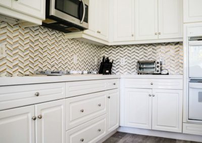 A newly remodeled kitchen featuring a new backsplash, custom white cabinets and new vinyl flooring.