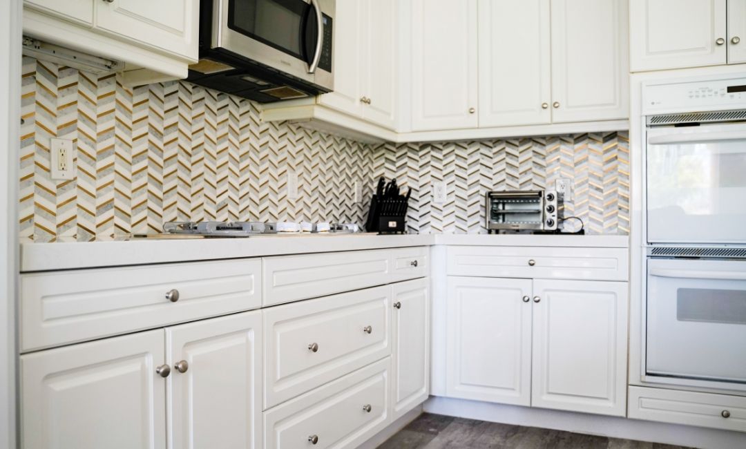 A newly remodeled kitchen that features a new herringbone patterned backsplash and custom white cabinets