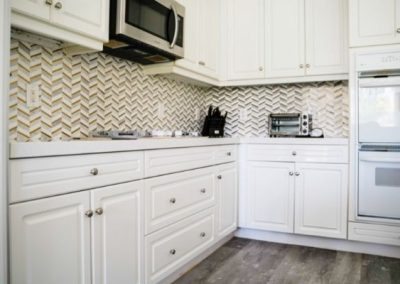 White kitchen cabinets, new flooring, and a unique herringbone backsplash that was created by Squared Construction during a kitchen remodel.